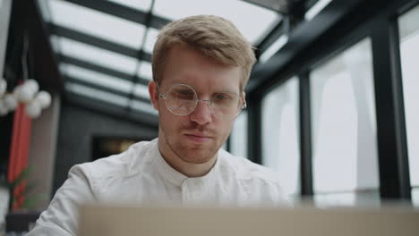 attractive-man-with-glasses-is-working-with-laptop-in-office-modern-coworking-space-for-freelancer-and-remote-worker